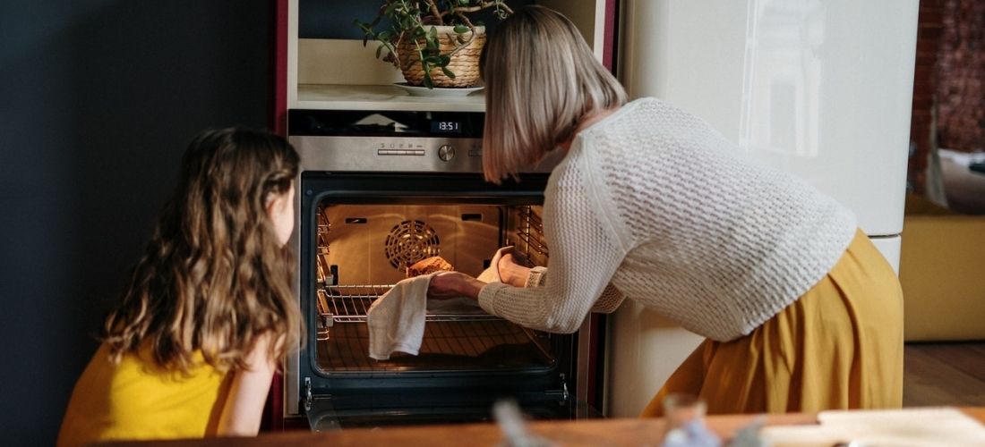 Mother and daughter place an item in the oven